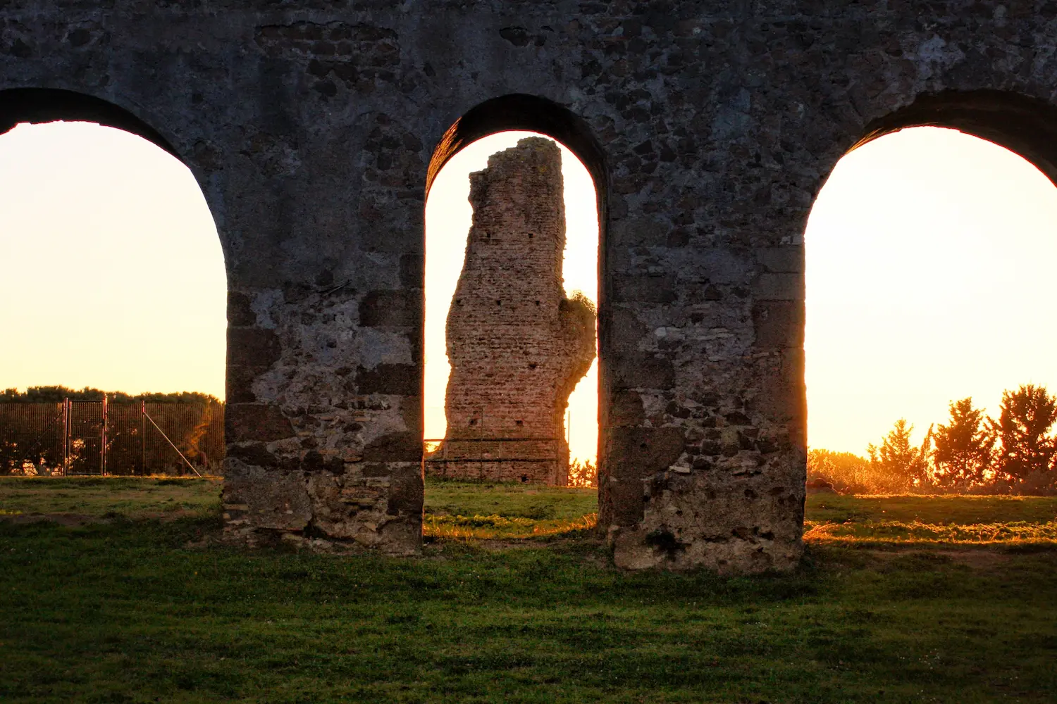 Three stone archways in an ancient ruin with golden sunset light passing through